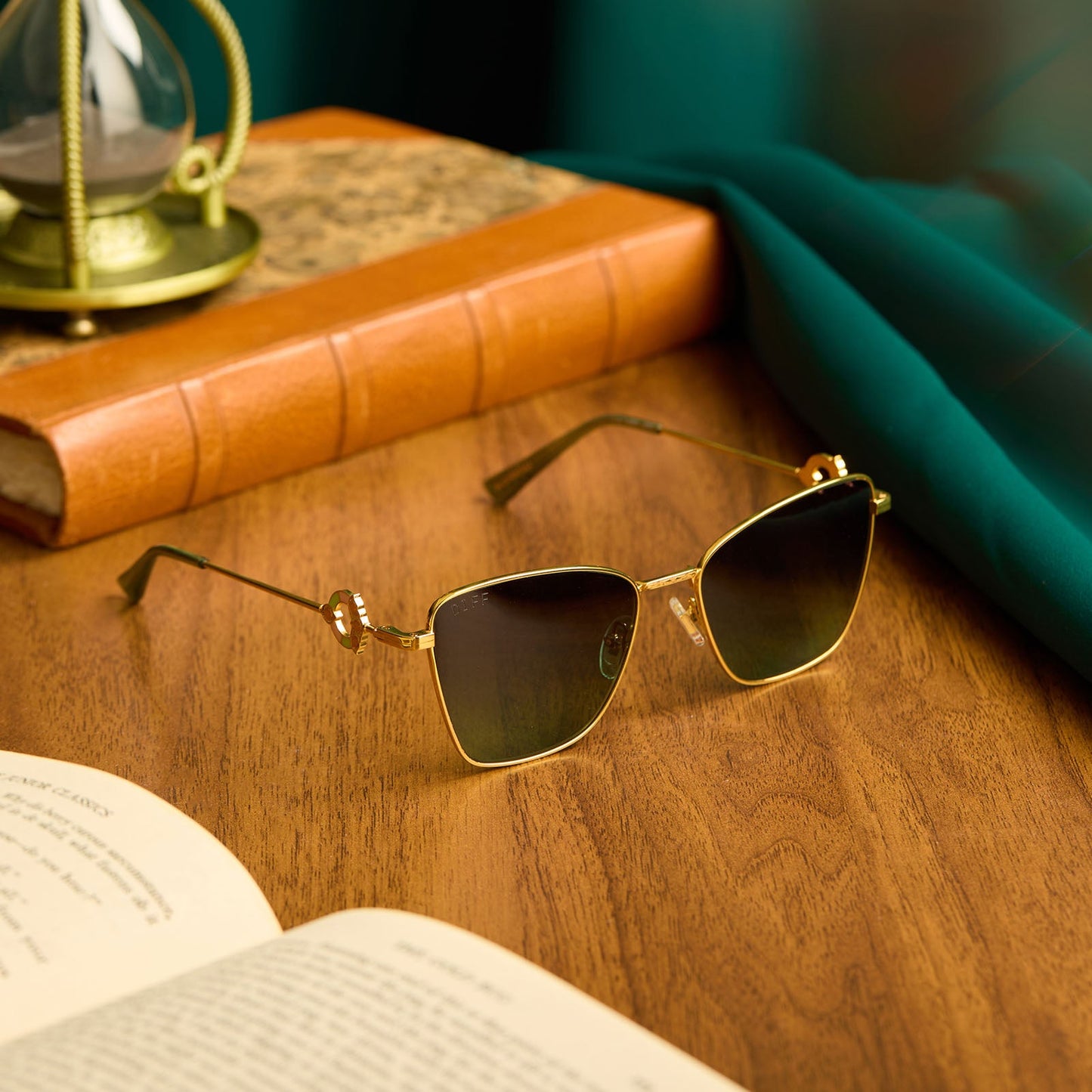 lifestyle - harry potter x diff eyewear featuring professor mcgonagall cat eye sunglasses with a gold frame and g15 lenses laying on a desk