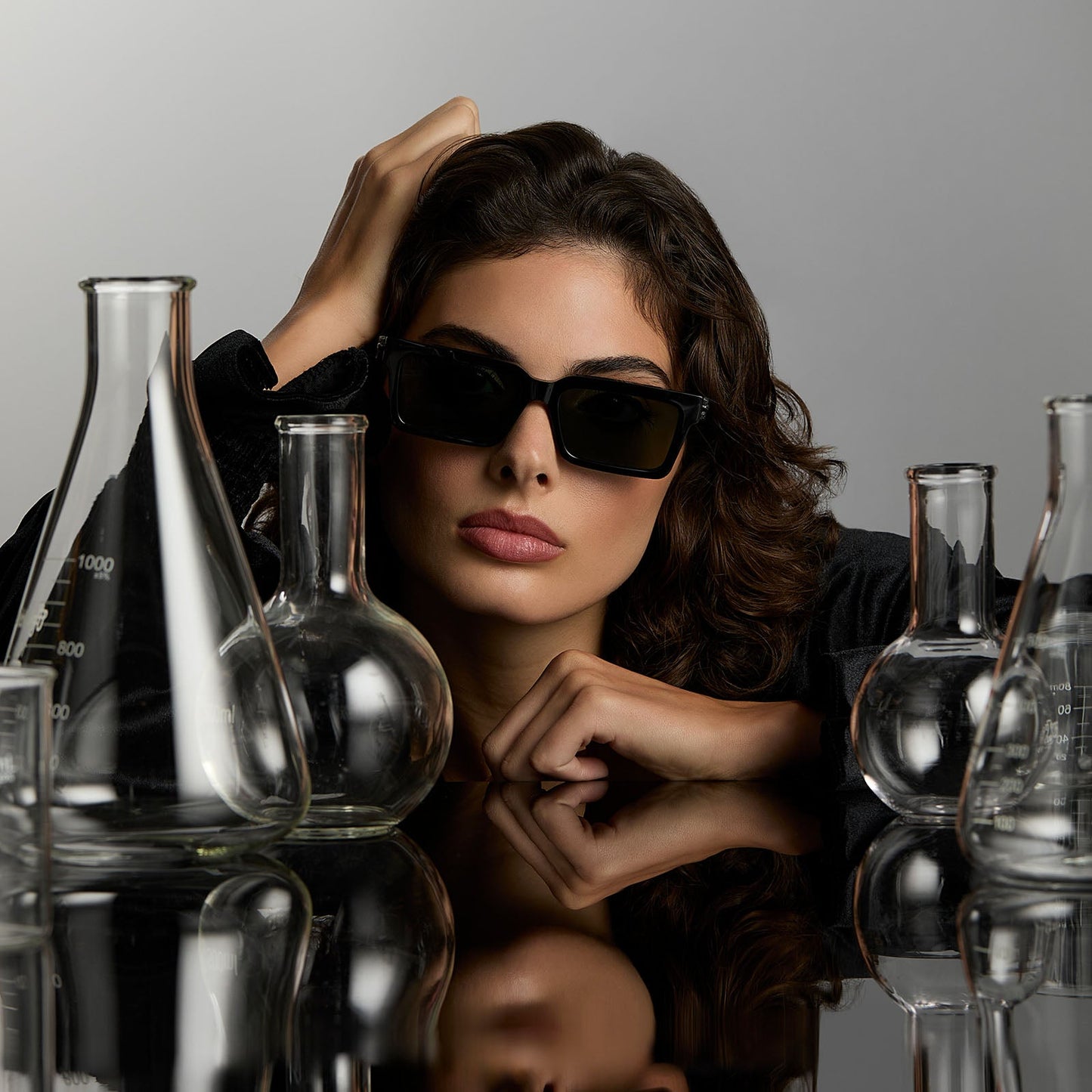 lifestyle - female surrounded by potion flask wearing harry potter x diff eyewear featuring professor snape 2.0 square sunglasses with a black frame and g15 lenses front view
