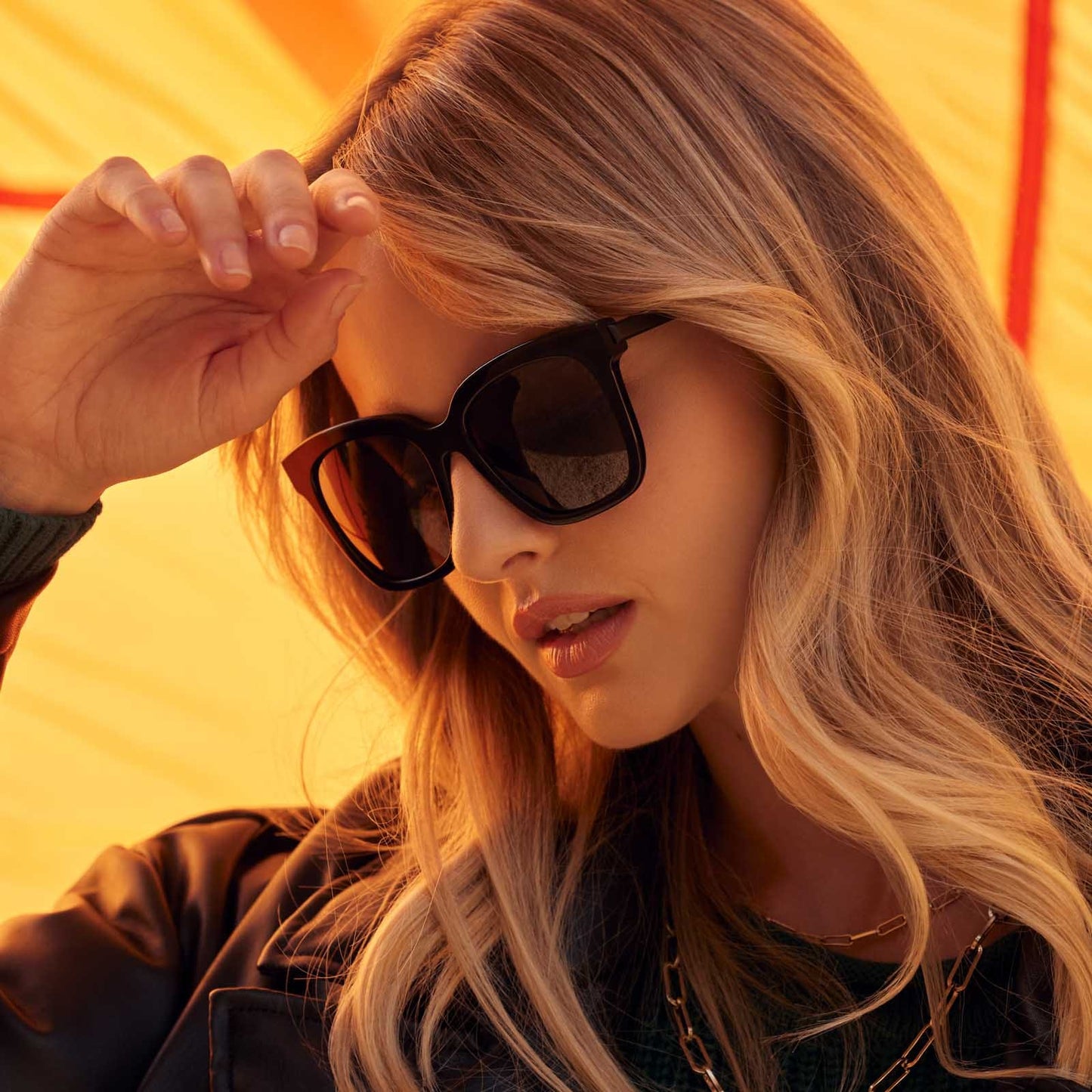 on model - blonde female with hand raised looking down wearing diff eyewear bella square sunglasses with a black acetate frame and grey polarized lenses