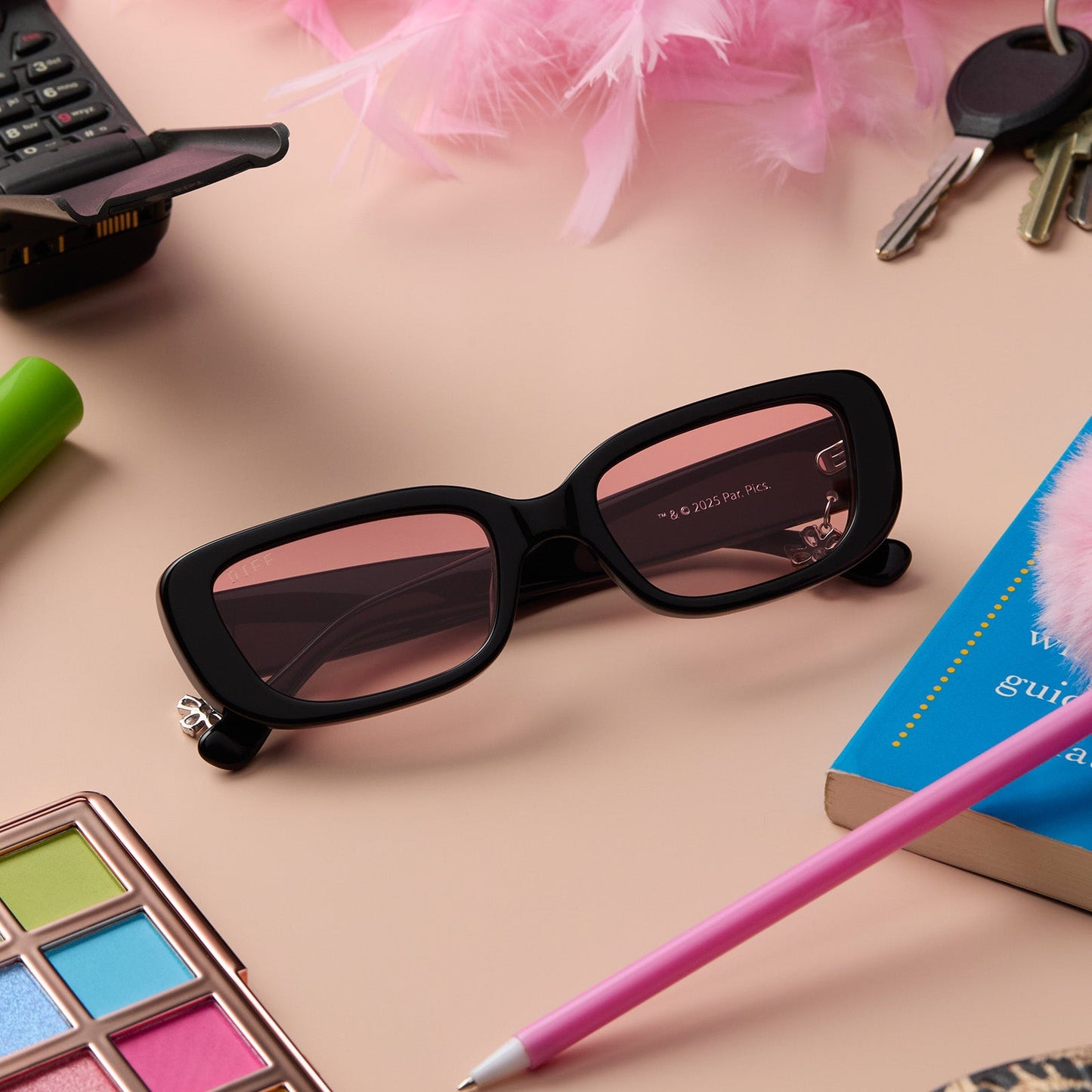 lifestyle - still life of clueless x diff eyewear featuring the cher round sunglasses with a black frame and pink gradient lenses front view