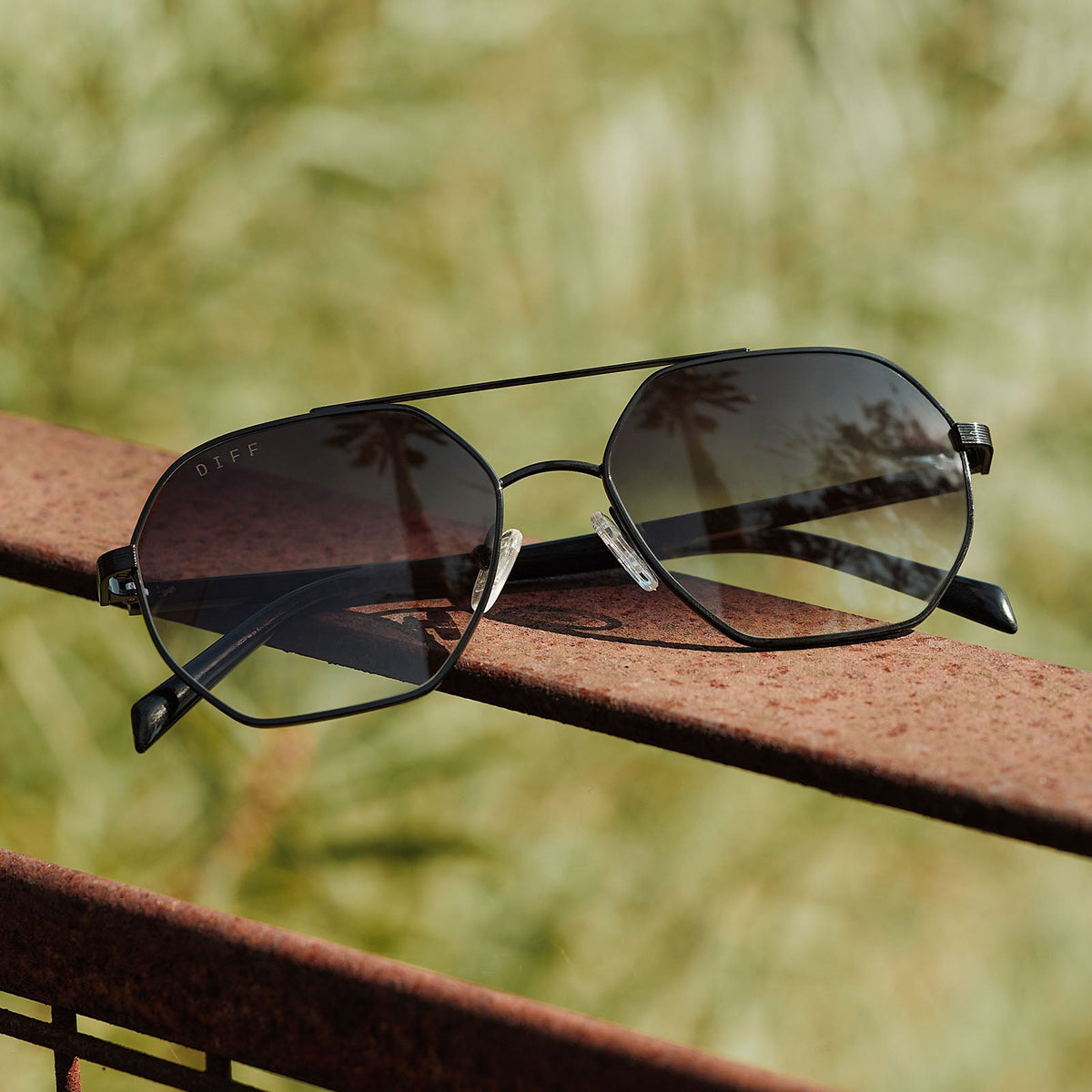 still life- jojo fletcher x diff eyewear joelle navigator sunglasses with a black metal frame and grey gradient lenses set on a railing