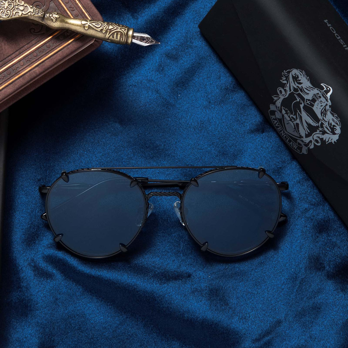 Flat-lay of Harry Potter x DIFF Ravenclaw sunglasses lying folded on top of blue fabric in front of tri-fold case