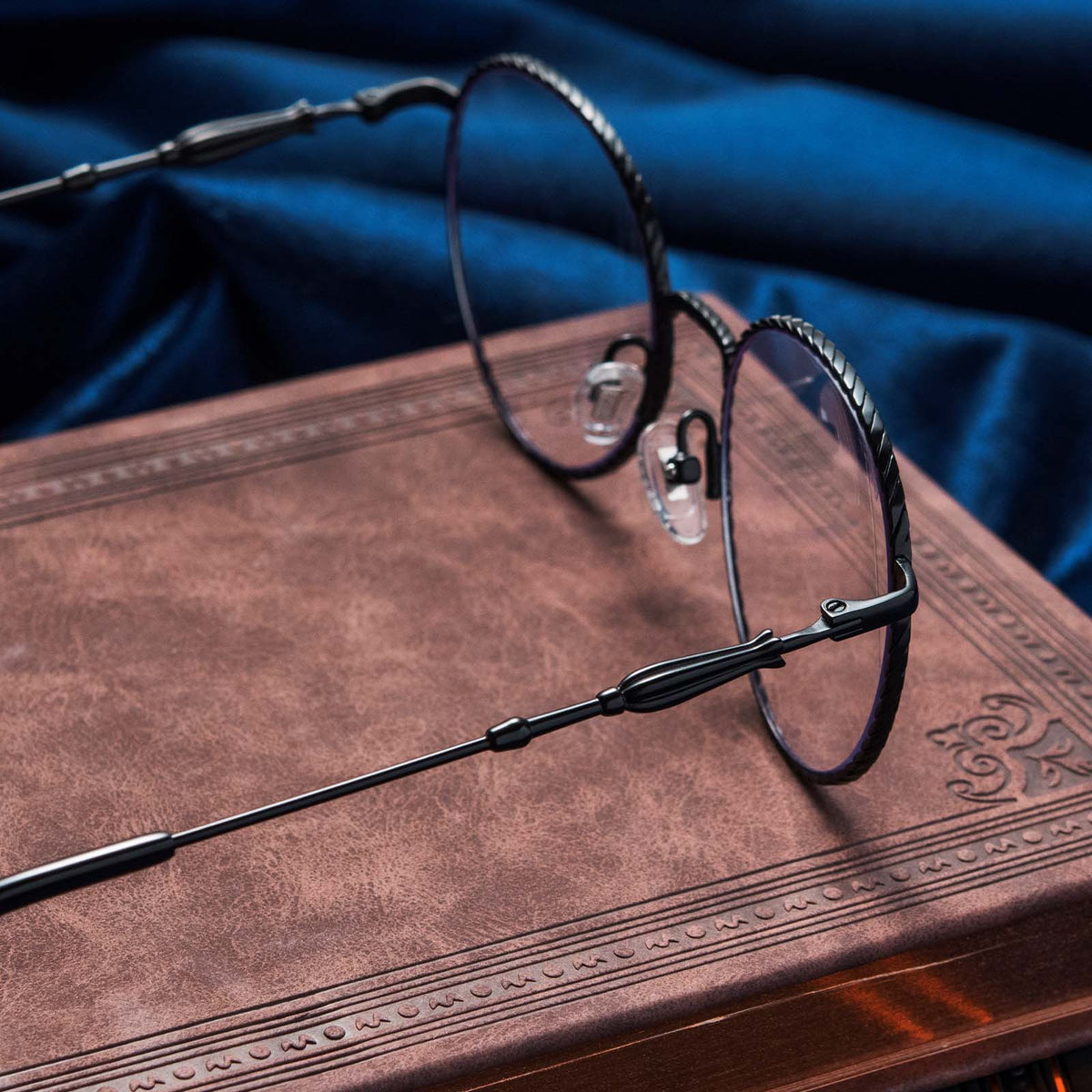 Harry Potter x DIFF Ravenclaw glasses lying open on top of book with blue fabric in the background