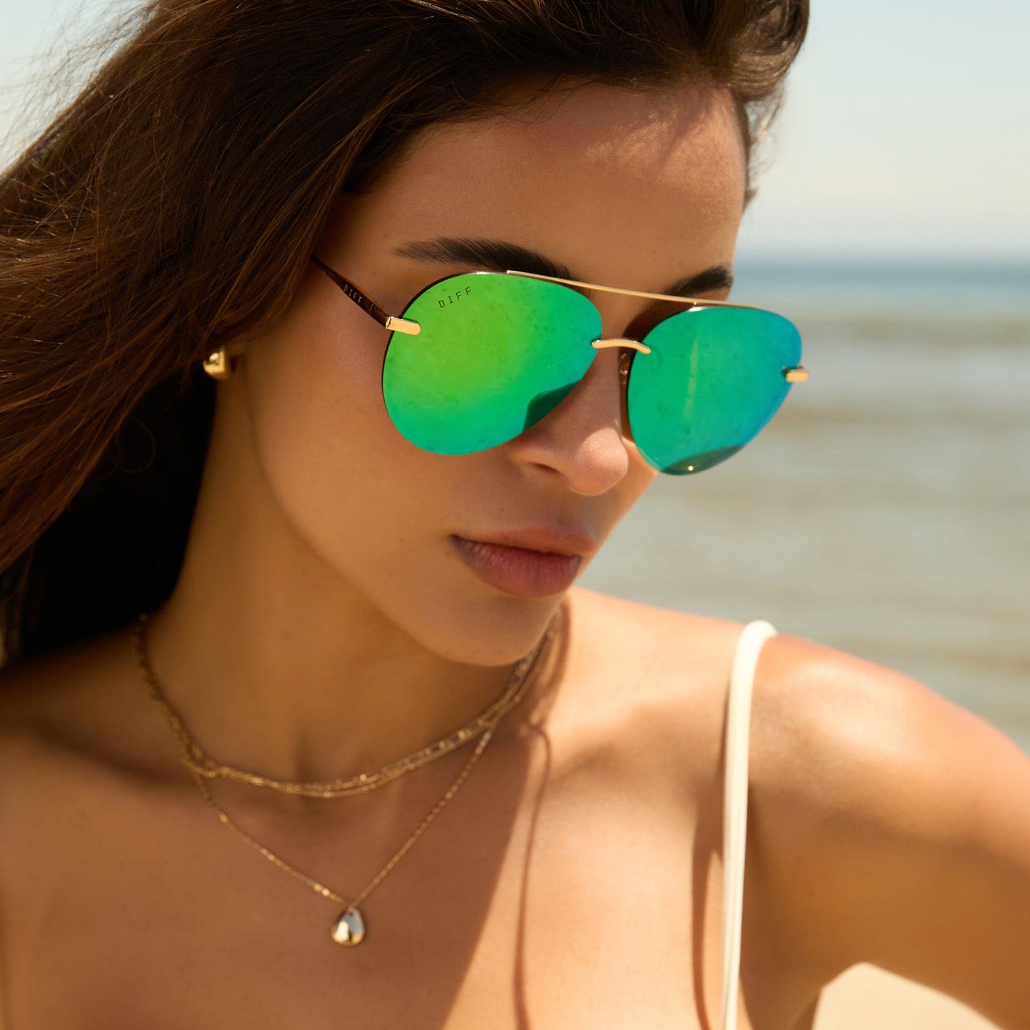 lifestyle - female while at the beach wearing diff eyewear lenox aviator sunglasses with a gold metal frame, green temple tips and green mirror polarized lenses angled view