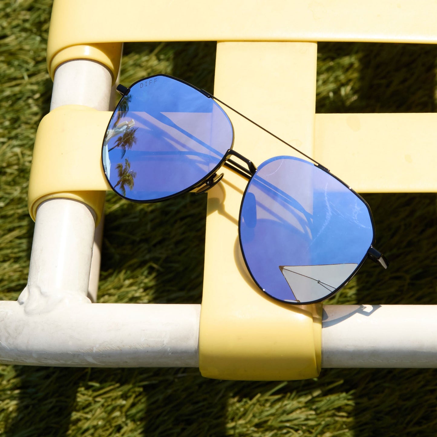 lifestyle - still life of diff eyewear dash black with lavender lenses sunglasses laying on a lawn chair