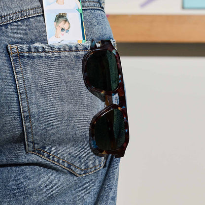 still life - jena sims x diff eyewear the sims navigator sunglasses with a blue color pop with gold metal frame and g15 polarized lenses hanging on her back pocket