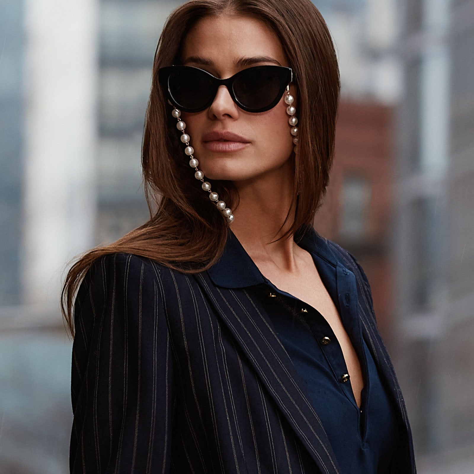 on model - business suited female  in NYC wearing devil wears prada x diff eyewear andy in black sunglasses with pearl chain.