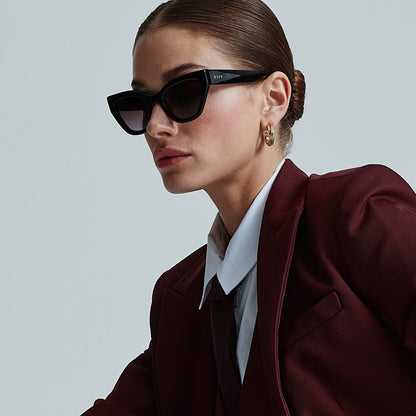 on model - female seated wearing devil wears prada x diff eyewear emily black acetate sunglasses