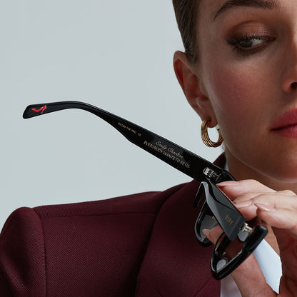 on model - female holding devil wears prada x diff eyewear emily black acetate sunglasses with a view of the inside of the temple showing the red stiletto shoe