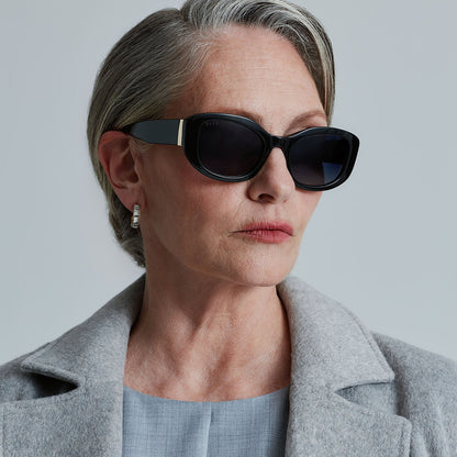 lifestyle - business suited woman wearing the devil wears prada x diff eyewear featuring the miranda square oversized sunglasses with a black acetate frame and grey gradient polarized lenses angled view