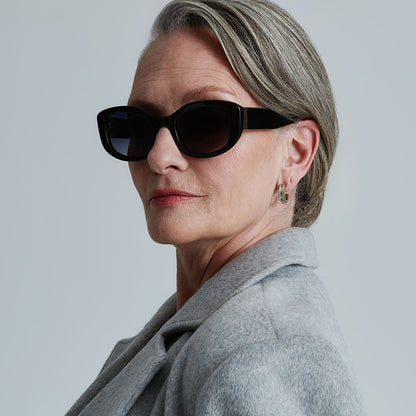 lifestyle - business suited woman wearing the devil wears prada x diff eyewear featuring the miranda square oversized sunglasses with a black acetate frame and grey gradient polarized lenses angled view