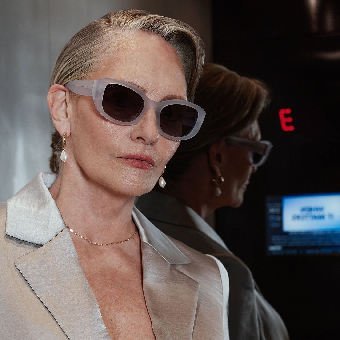 lifestyle - business female in an elevator wearing the devil wears prada x diff eyewear featuring the miranda square oversized sunglasses with a milky white acetate frame and grey gradient polarized lenses front view
