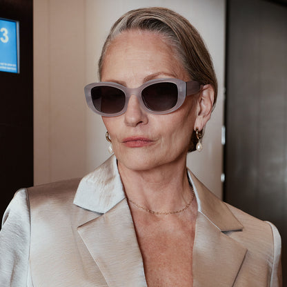 lifestyle - business female in an elevator wearing the devil wears prada x diff eyewear featuring the miranda square oversized sunglasses with a milky white acetate frame and grey gradient polarized lenses front view