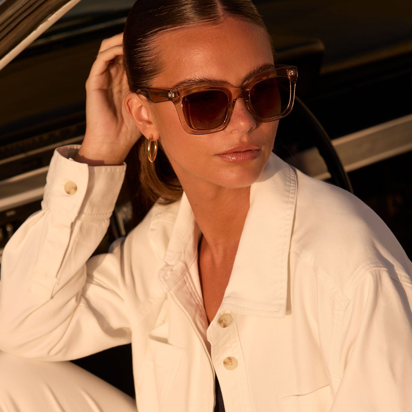 lifestyle - female lounging in a car wearing travis mathews x diff eyewear the valencia square sunglasses with a soft taupe crystal acetate frame and brown gradient polarized lenses angled view