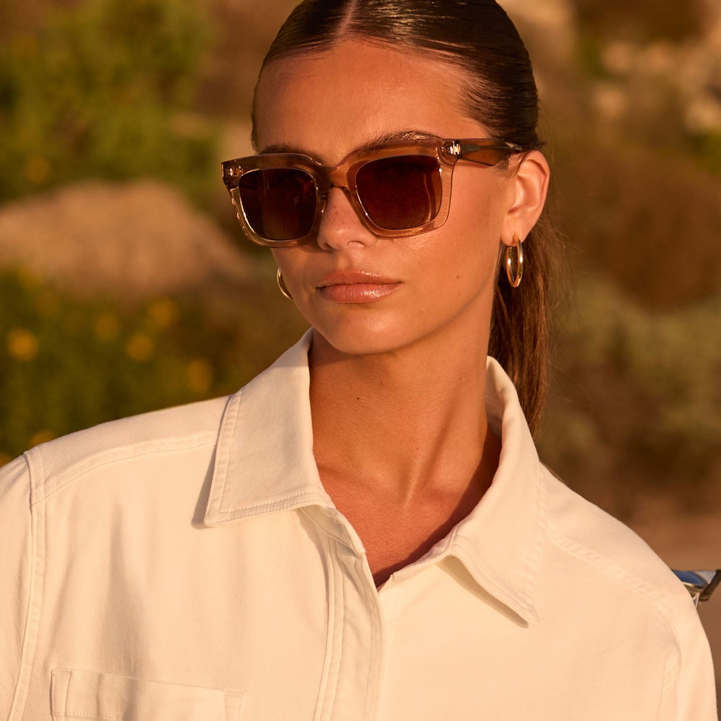 lifestyle - female outdoors wearing travis mathews x diff eyewear the valencia square sunglasses with a soft taupe crystal acetate frame and brown gradient polarized lenses front view