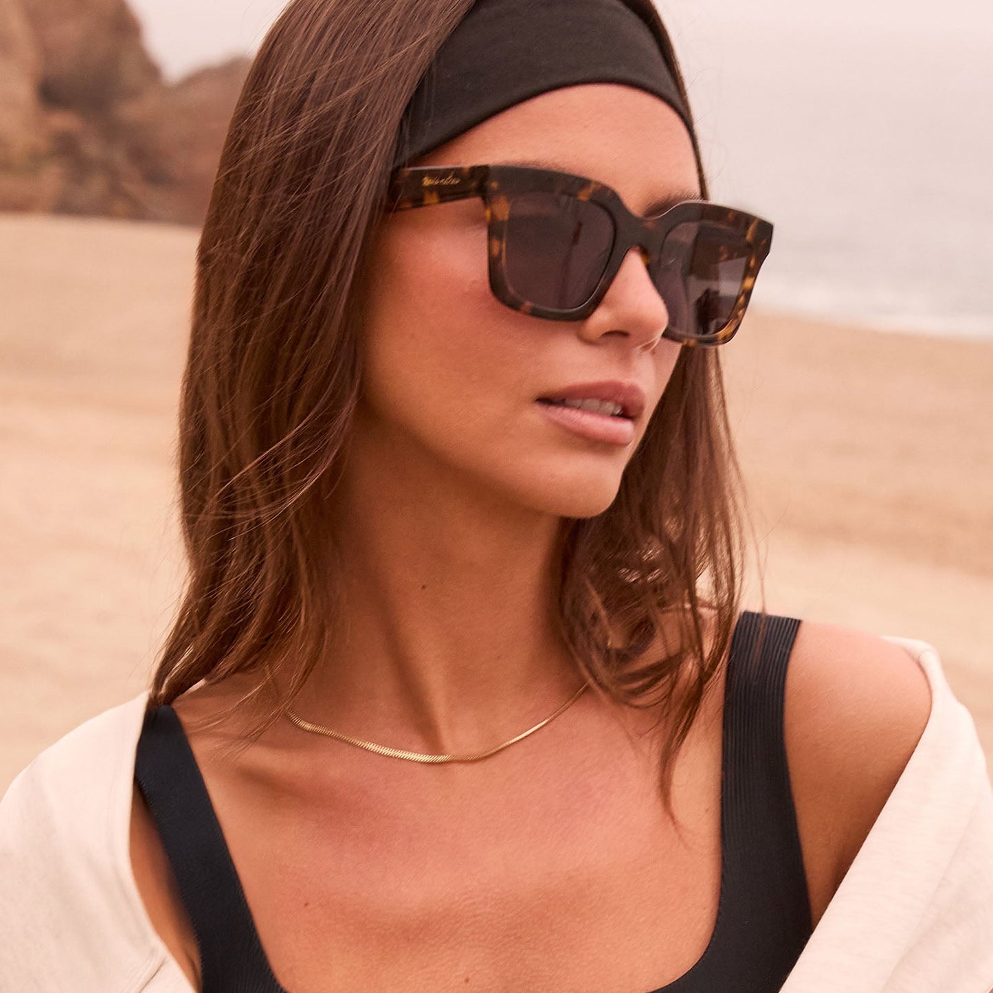 lifestyle - female at the beach wearing travis mathews x diff eyewear the valencia square sunglasses with a tortoise acetate frame and grey polarized lenses angled view