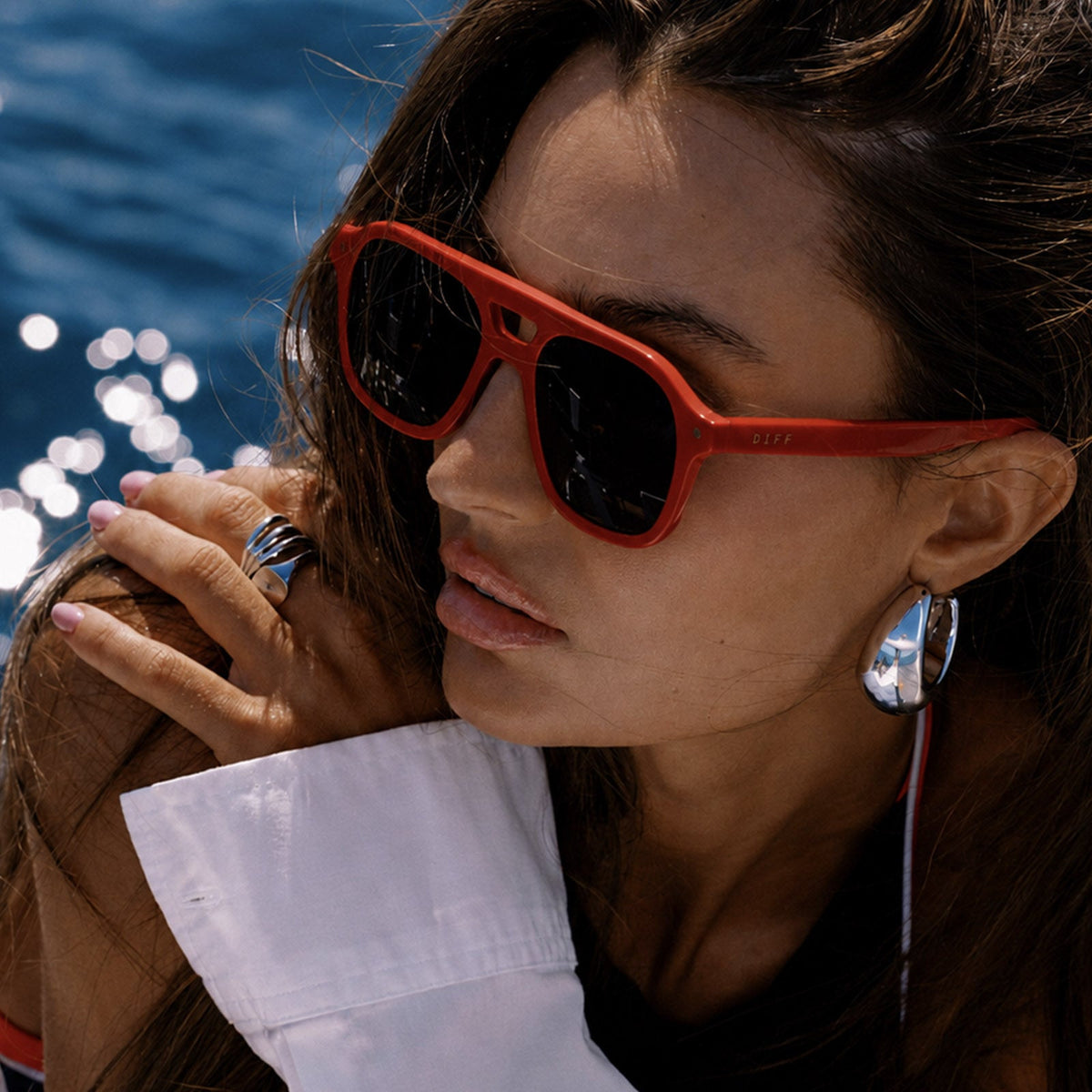 lifestyle - female on a boat wearing beach riot x diff eyewear the coast navigator sunglasses with a red acetate frame and navy blue lenses angled view