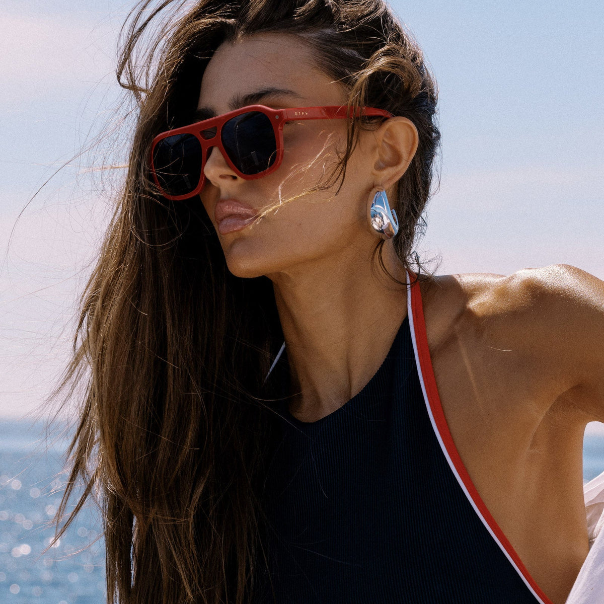 lifestyle - female on a boat wearing beach riot x diff eyewear the coast navigator sunglasses with a red acetate frame and navy blue lenses side view