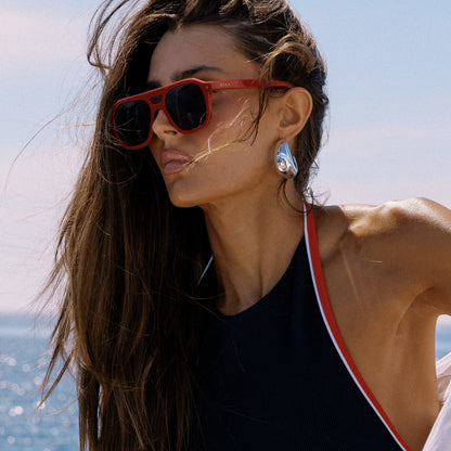 lifestyle - female on a boat wearing beach riot x diff eyewear the coast navigator sunglasses with a red acetate frame and navy blue lenses side view