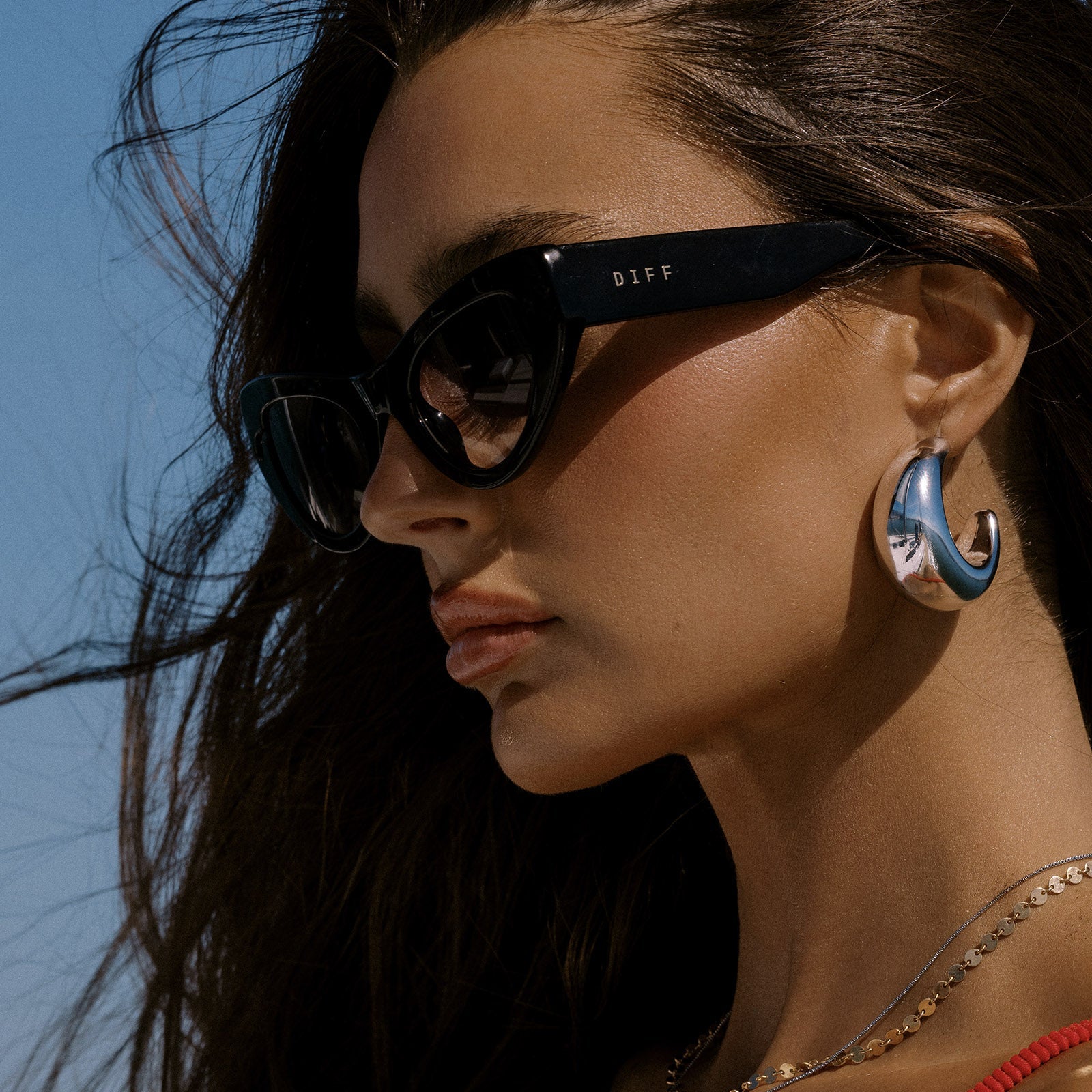 lifestyle - female at the beach wearing beach riot x diff eyewear the mesa cat eye sunglasses with a black acetate frame and grey gradient lenses side view