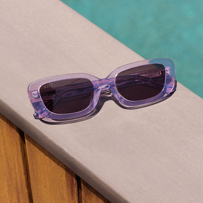 still life - diff eyewear daphne ii low profile square sunglasses with a lilac crystal purple acetate frame laying by the pool