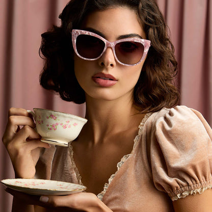 lifestyle - female drinking tea wearing harry potter x diff eyewear featuring professor umbridge cat eye sunglasses with a pink mother of pearl frame and wine gradient lenses front view