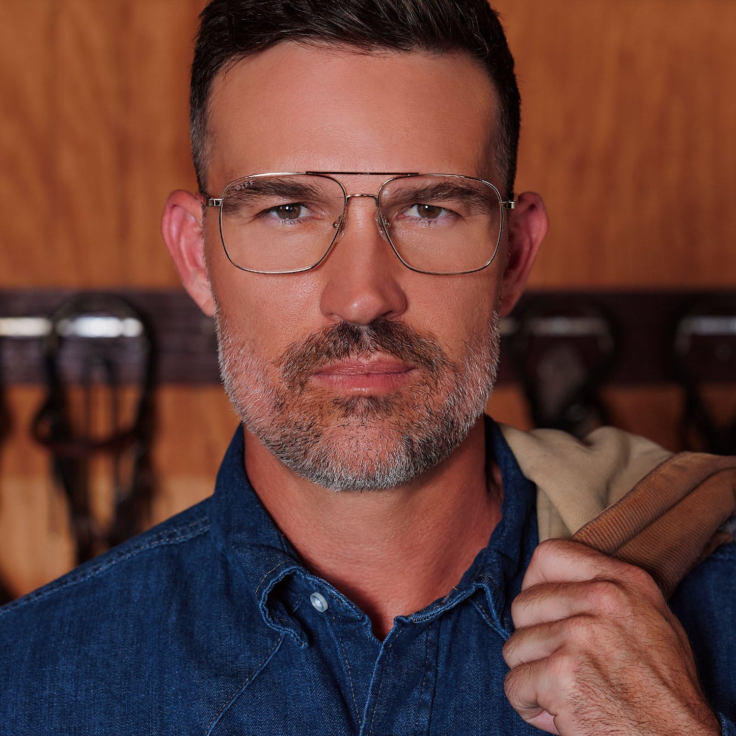 lifestyle - male in horse stable wearing yellowstone x diff eyewear featuring the rip wheeler navigator prescription glasses with a gold frame front view