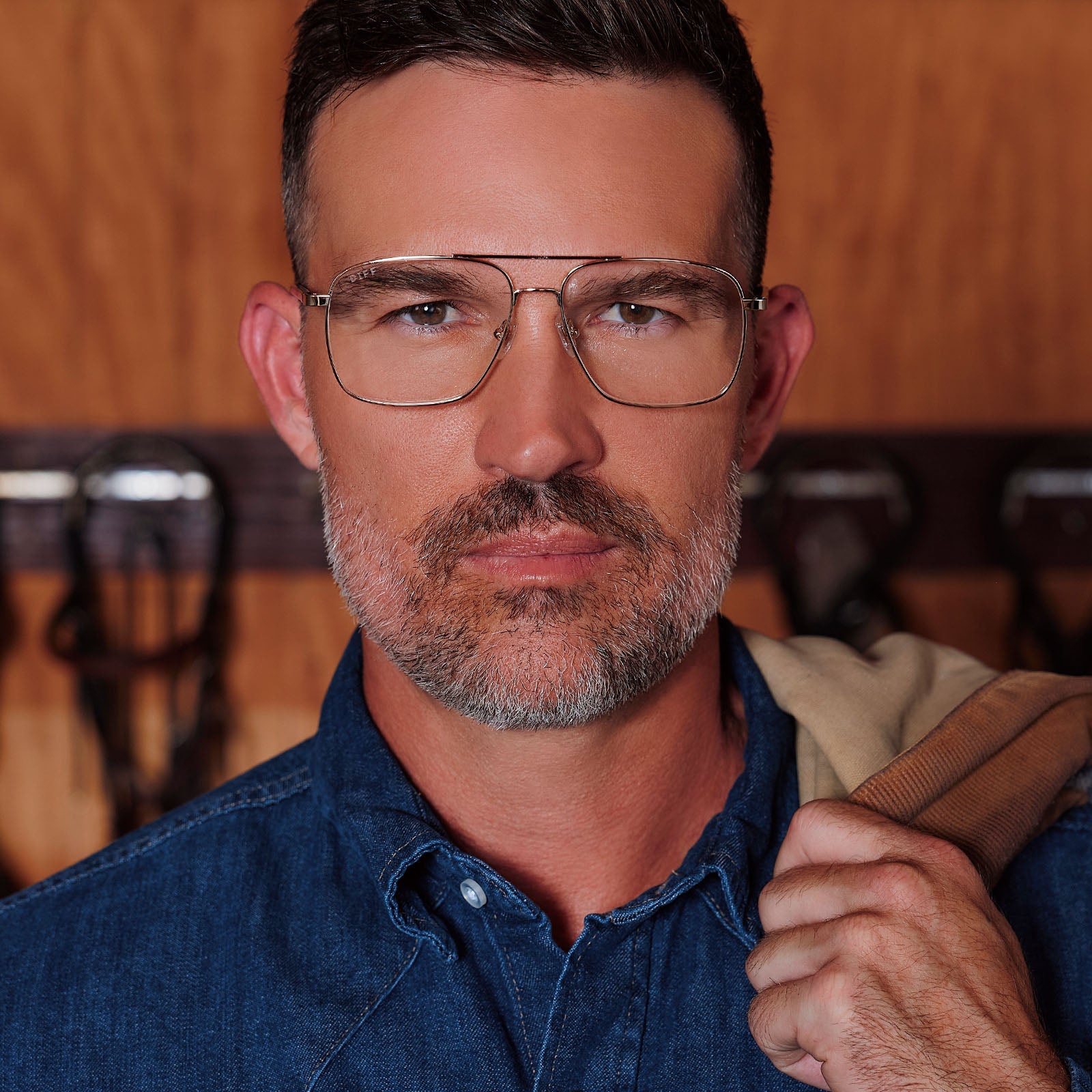 lifestyle - male in horse stable wearing yellowstone x diff eyewear featuring the rip wheeler navigator prescription glasses with a gold frame front view