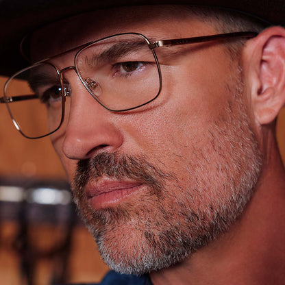 lifestyle - male in horse stable wearing yellowstone x diff eyewear featuring the rip wheeler navigator prescription glasses with a gold frame detailed view