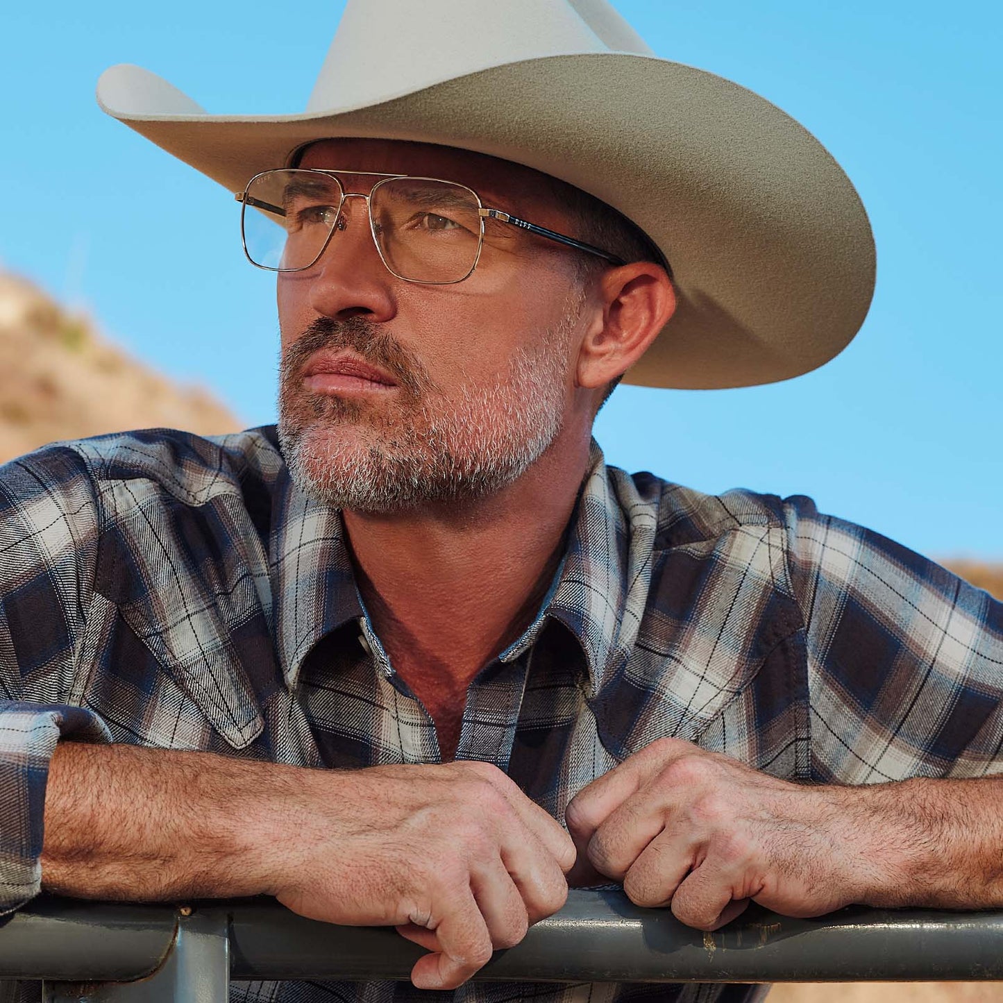 lifestyle - male at horse ranch wearing yellowstone x diff eyewear featuring the rip wheeler navigator prescription glasses with a silver frame angled view