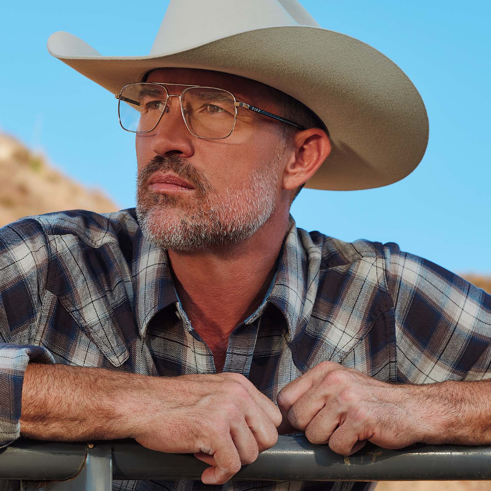 lifestyle - male at horse ranch wearing yellowstone x diff eyewear featuring the rip wheeler navigator prescription glasses with a silver frame angled view