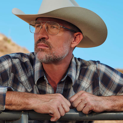 lifestyle - male at horse ranch wearing yellowstone x diff eyewear featuring the rip wheeler navigator prescription glasses with a silver frame angled view