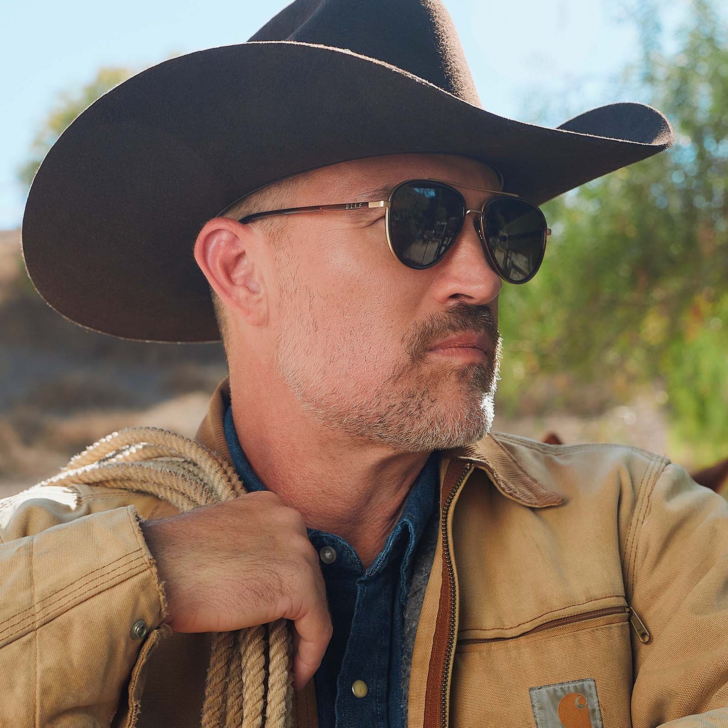 lifestyle - male in a cowboy hat wearing yellowstone x diff eyewear featuring the yellowstone aviator sunglasses with a sequoia tortoise frame and brown polarized lenses side view