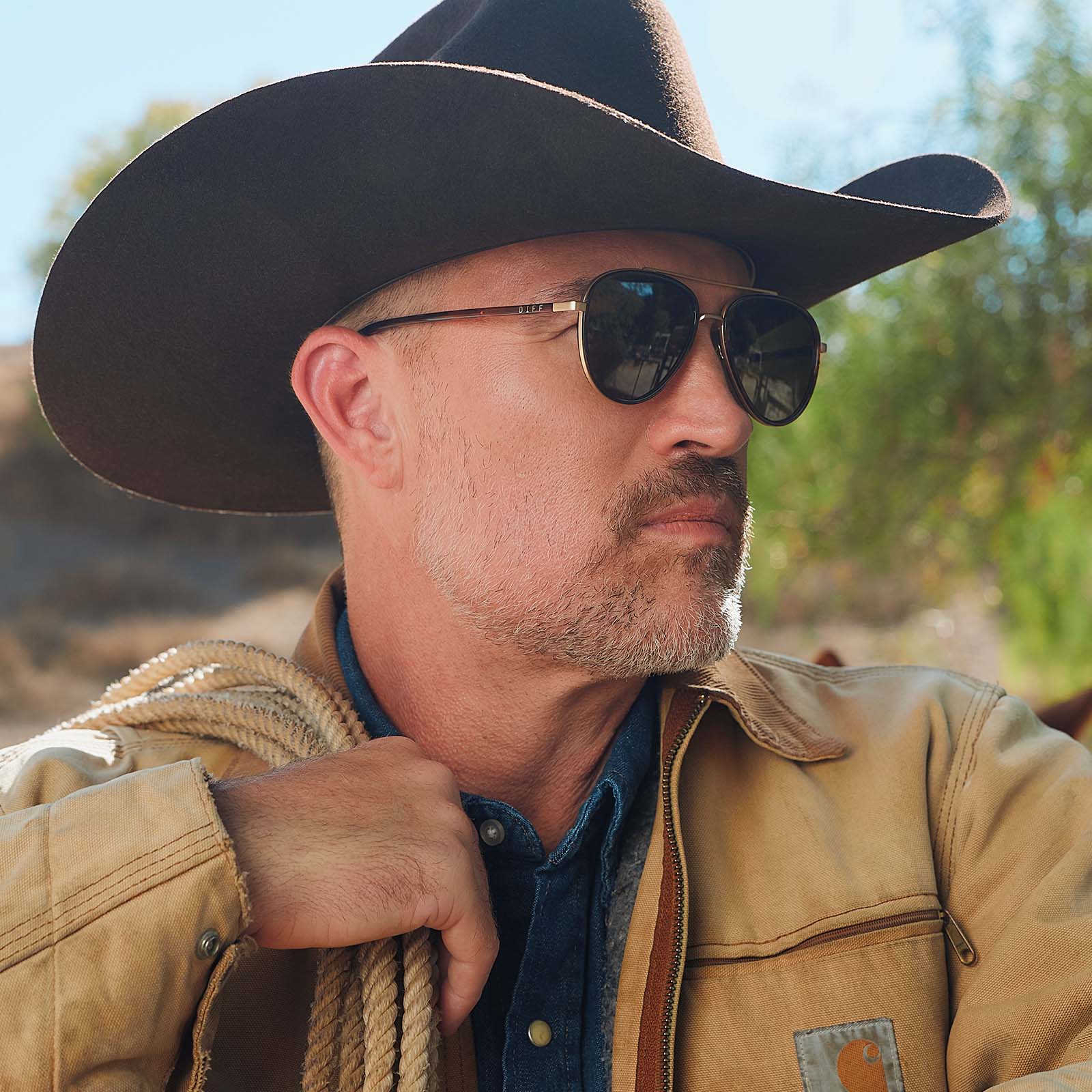 lifestyle - male in a cowboy hat wearing yellowstone x diff eyewear featuring the yellowstone aviator sunglasses with a sequoia tortoise frame and brown polarized lenses side view