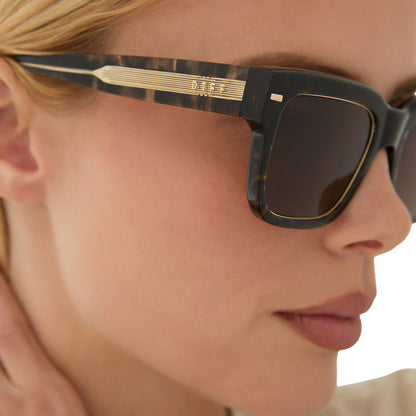 lifestyle - female wearing emily in paris x diff eyewear featuring the alfie rectangle sunglasses with a truffle tortoise frame and deep brown lenses side view 