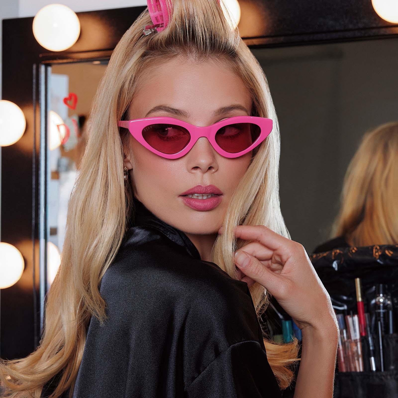 lifestyle - female in preping in studio wearing emily in paris x diff eyewear featuring the emily 2.0 cateye sunglasses with a parisian pink frame and maracon pink lenses front view