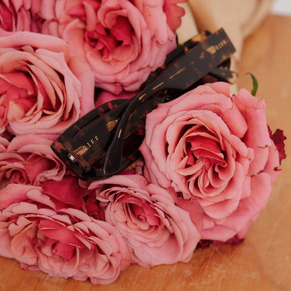still life of boutique of flowers with emily in paris x diff eyewear featuring the julien 2.0 rectangle sunglasses with a classic tortoise frame and warm brown lenses