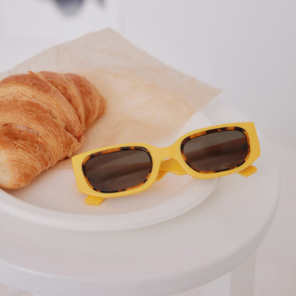 still life of emily in paris x diff eyewear featuring the julien 2.0 rectangle sunglasses with a citron yellow with tortoise frame and chic grey lenses laying next to a french croissant