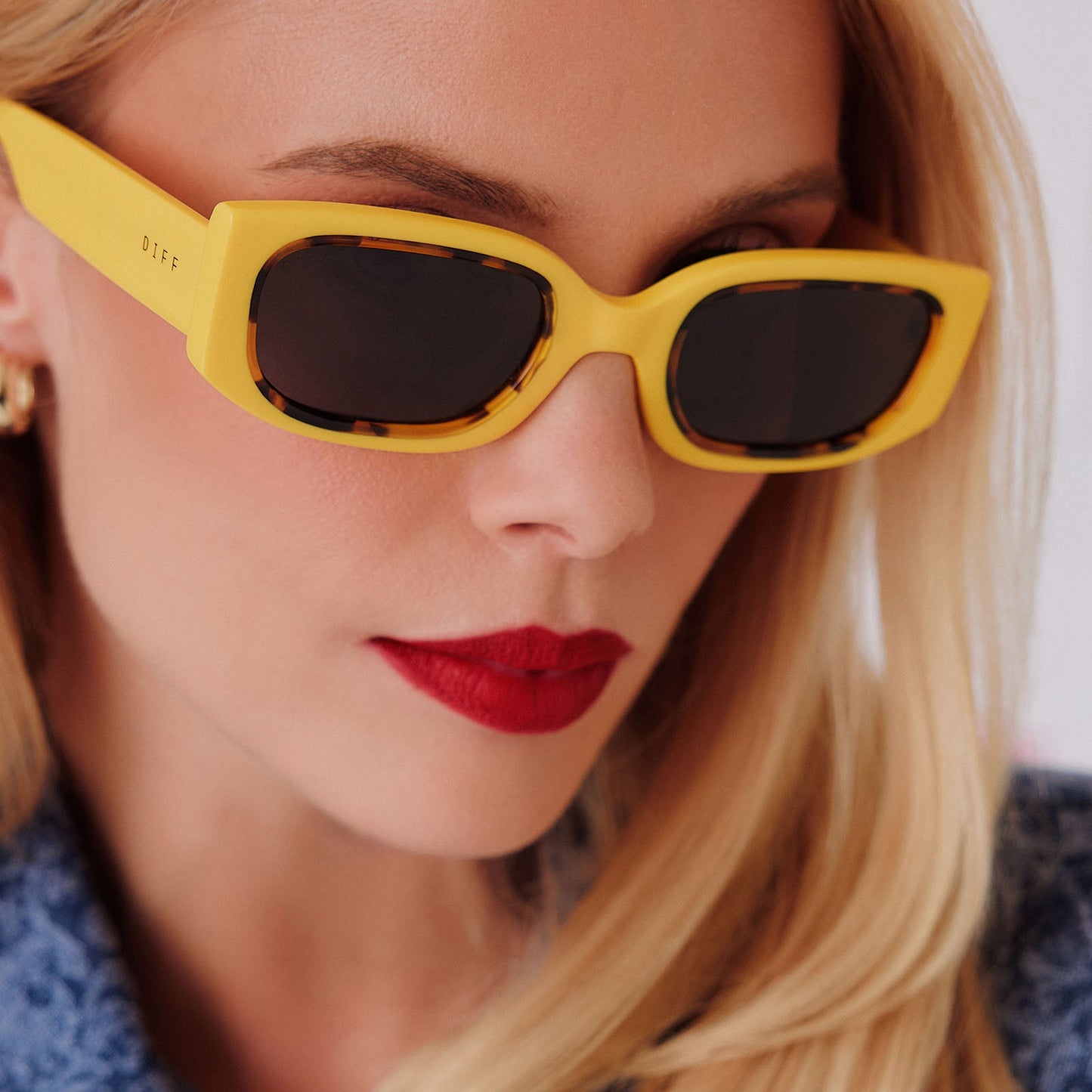 lifestyle - female in photo studio trying on emily in paris x diff eyewear featuring the julien 2.0 rectangle sunglasses with a citron yellow with tortoise frame and chic grey lenses detailed view