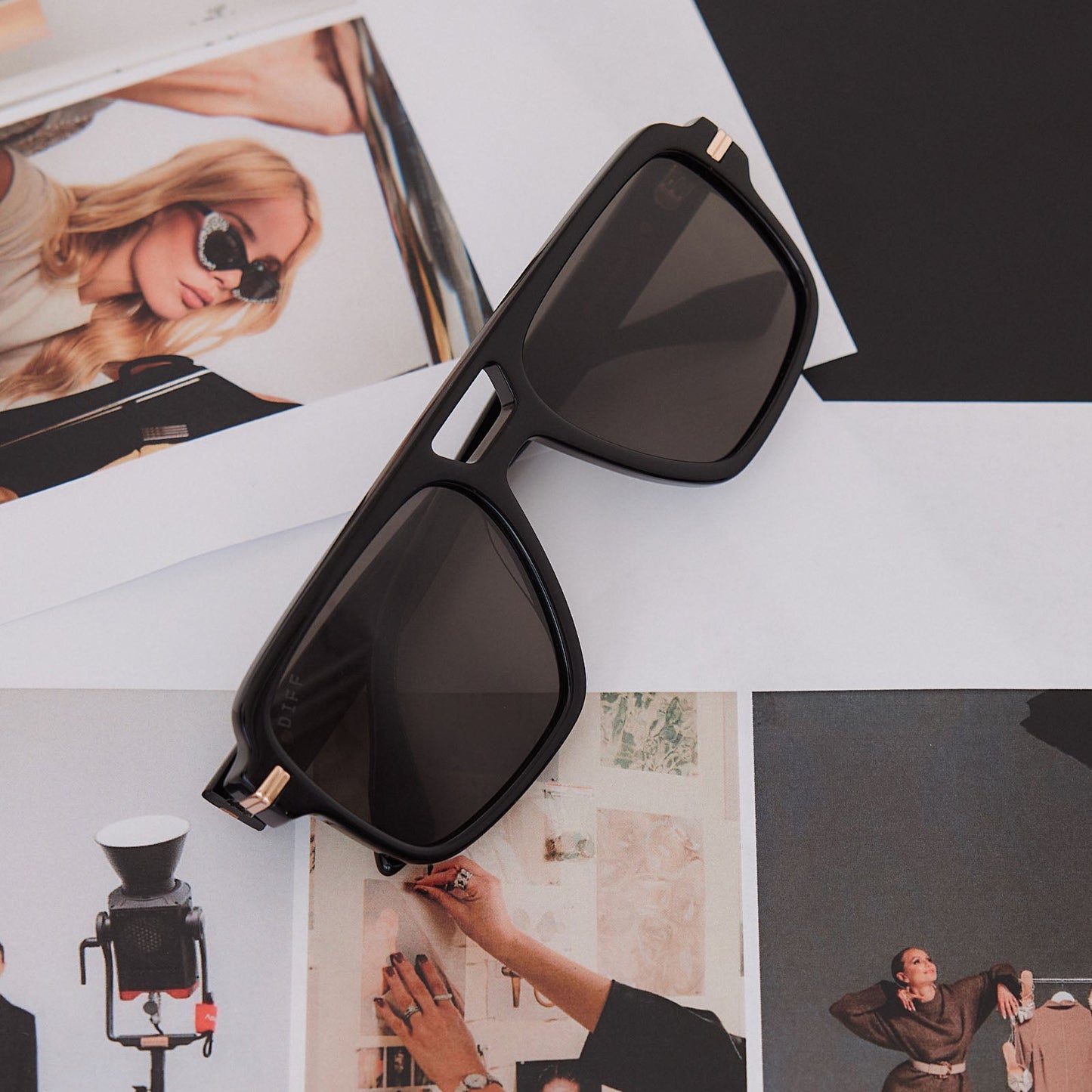 still life of emily in paris x diff eyewear featuring the julien navigator sunglasses with a jet noir black frame and smoke black lenses on a photo desk