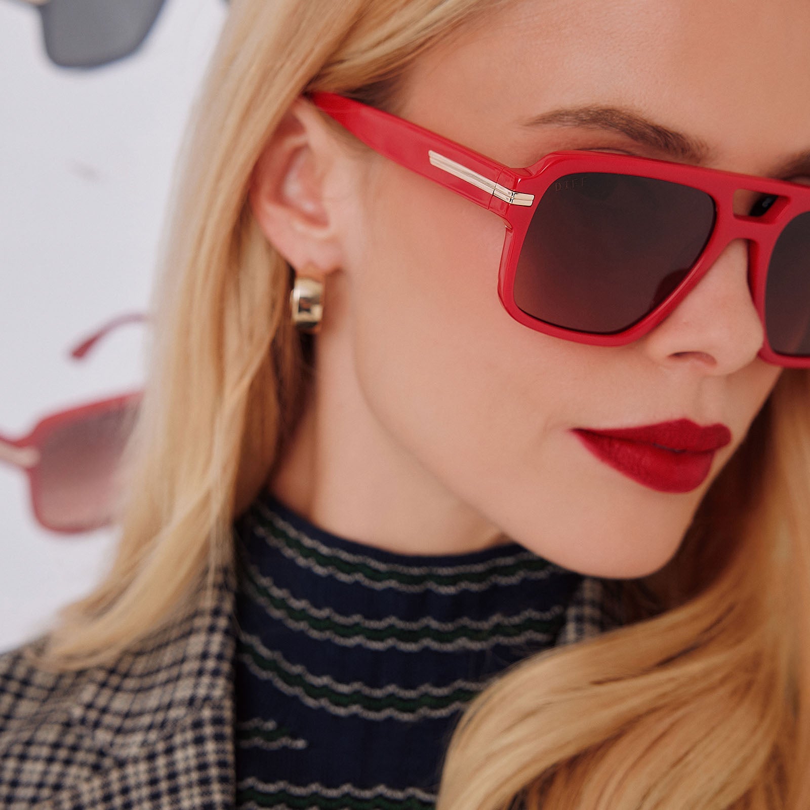 lifestyle - female in photo studio trying on emily in paris x diff eyewear featuring the julien navigator sunglasses with a rouge vogue red frame and warm brown gradient lenses side view