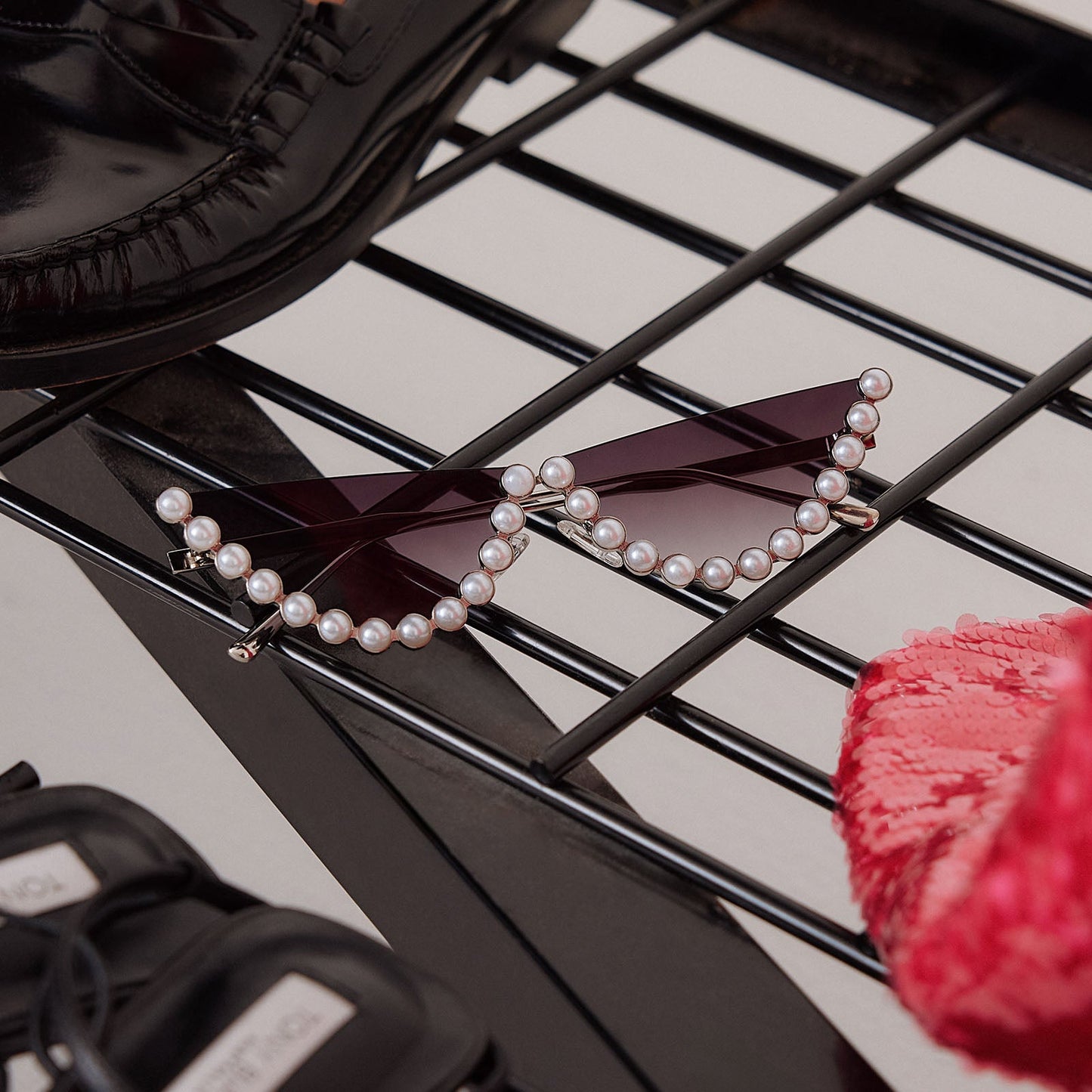 still life of emily in paris x diff eyewear featuring the mindy 2.0 cateye sunglasses with a champagne pearl frame and grey gradient lenses next to accessories and shoes