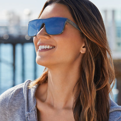 lifestyle - female in front of a pier wearing diff sport flash square sunglasses with a slate grey frame and grey gradient with silver flash polarized lenses front view