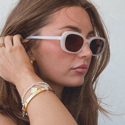 lifestyle - aspyn ovard x diff eyewear female wearing the cove oval sunglasses with a milky blush frame and brown lenses side view