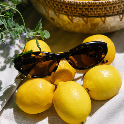 flat lay of jessie james decker x diff eyewear featuring the dolce bella oval sunglasses with a espresso tortoise frame and brown lenses top view