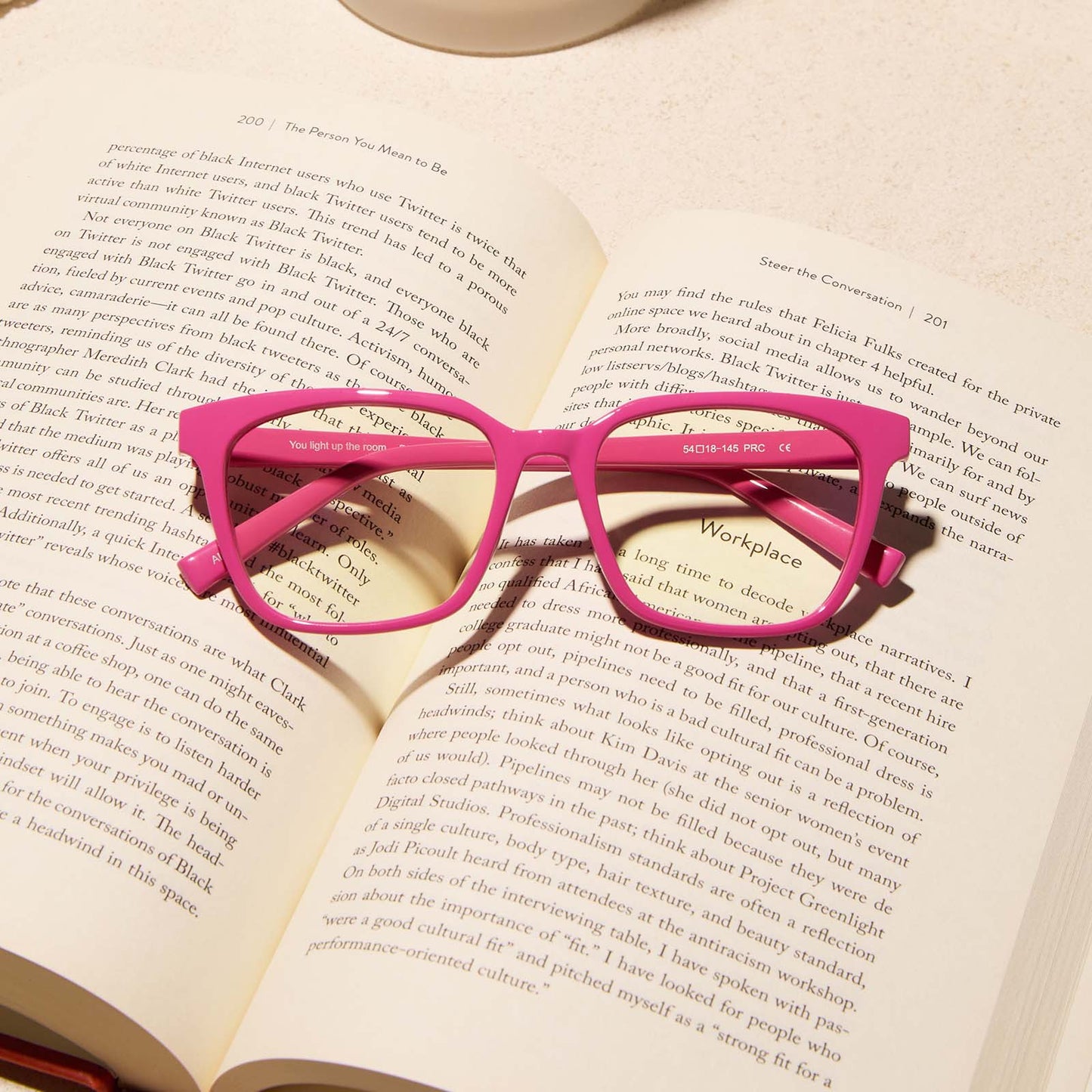 lifestyle - diff eyewear featuring the alex square blue light readers with a peony pink frame laying on a book