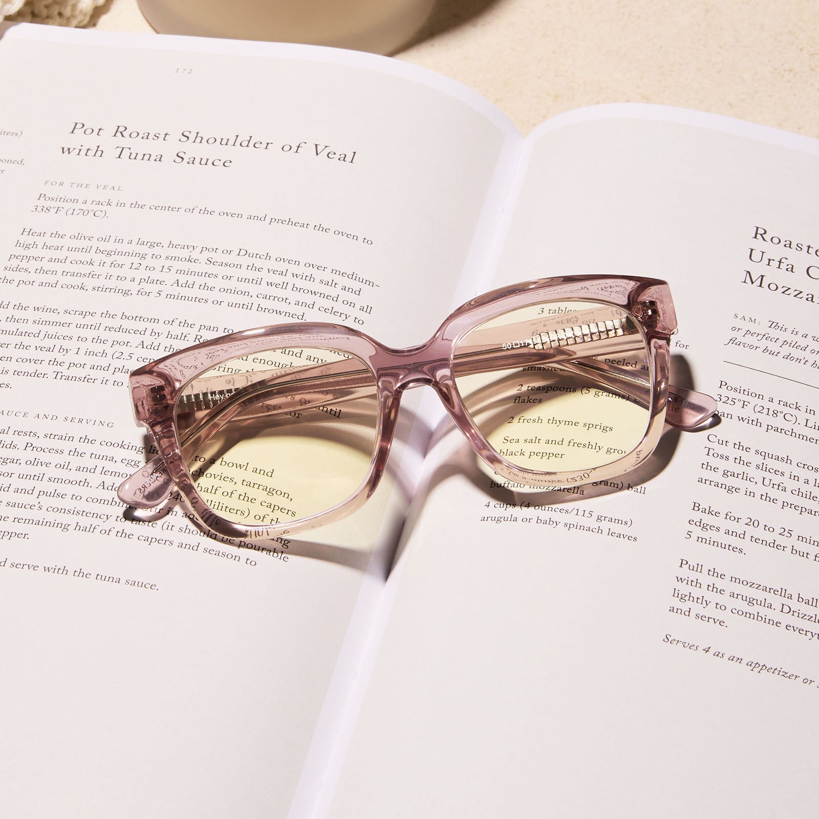 lifestyle - diff eyewear featuring the ava square blue light readers with a light pink crystal frame laying on a book