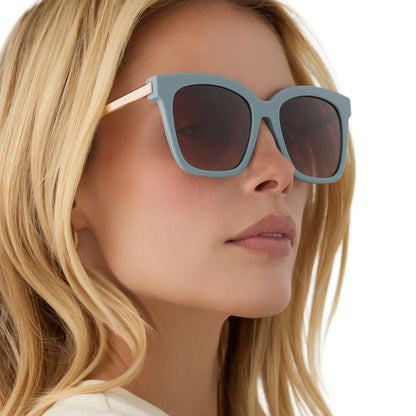 on model - blonde female wearing diff eyewear bella square oversized sunglasses with a dew drop blue frame, gold temples and brown gradient lenses side view