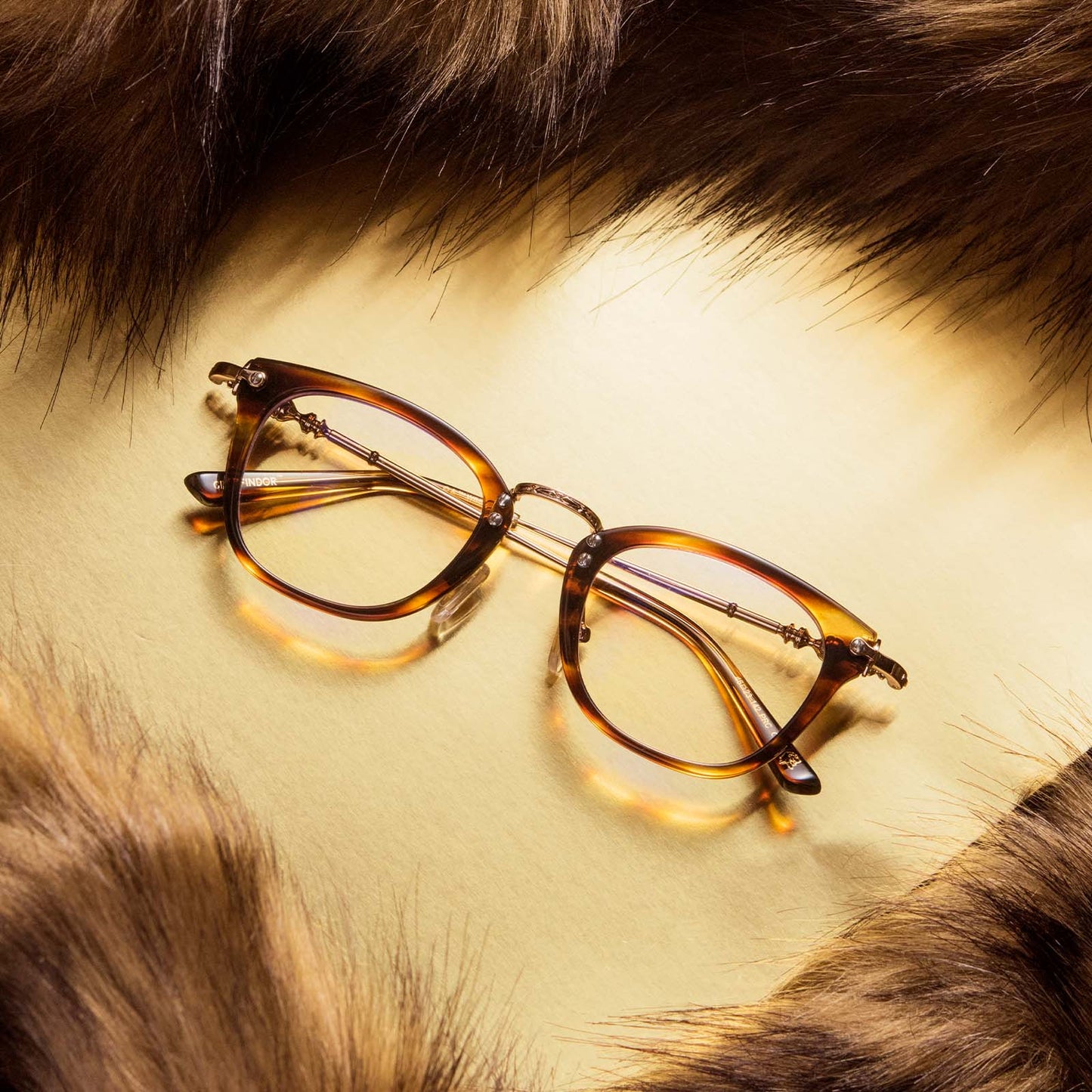 Flat-lay of Harry Potter x DIFF Gryffindor glasses lying folded on yellow background encircled by brown fabric