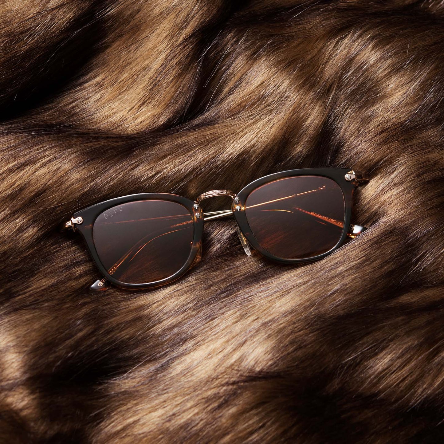Flat-lay of Harry Potter x DIFF Gryffindor sunglasses lying folded on top of brown fabric